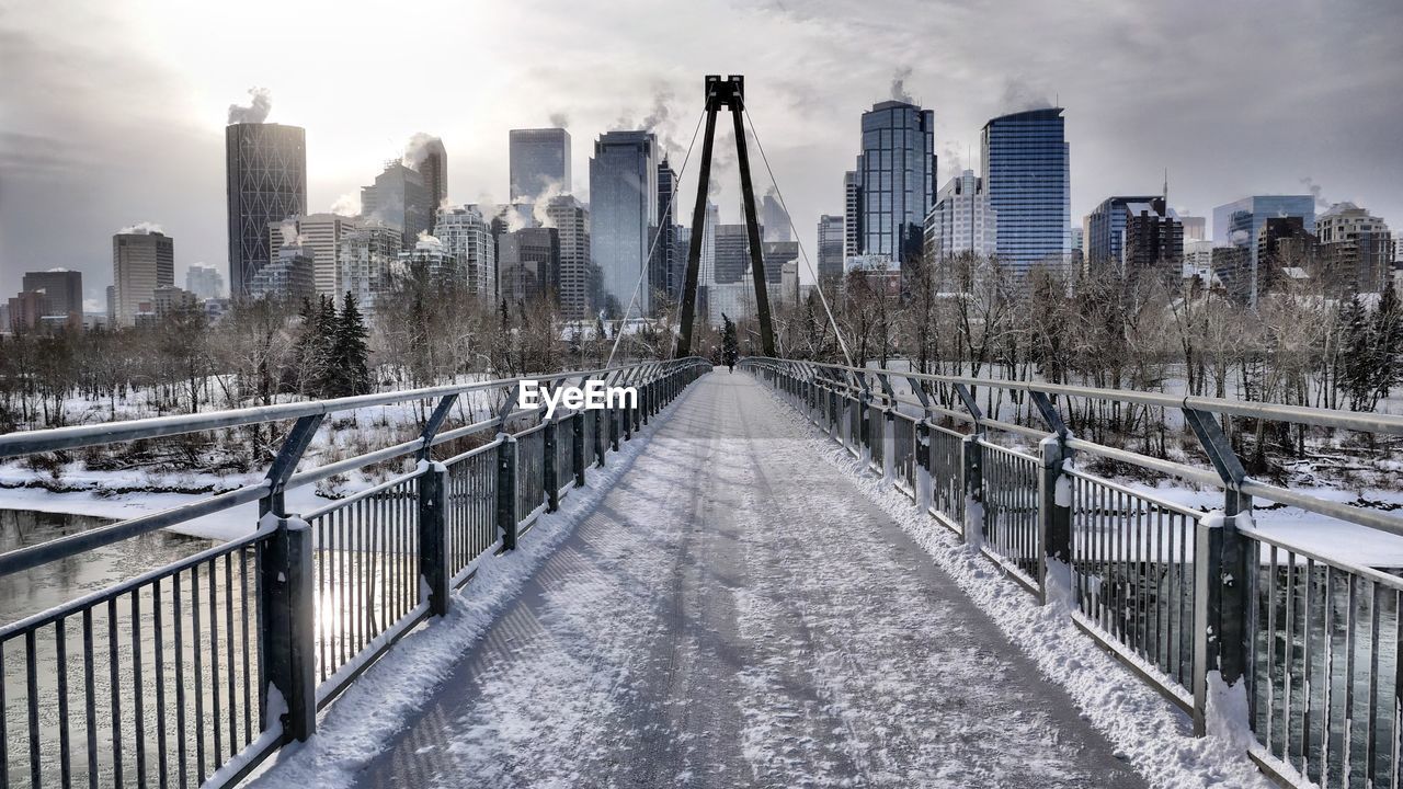 Snow covered footbridge amidst buildings in city