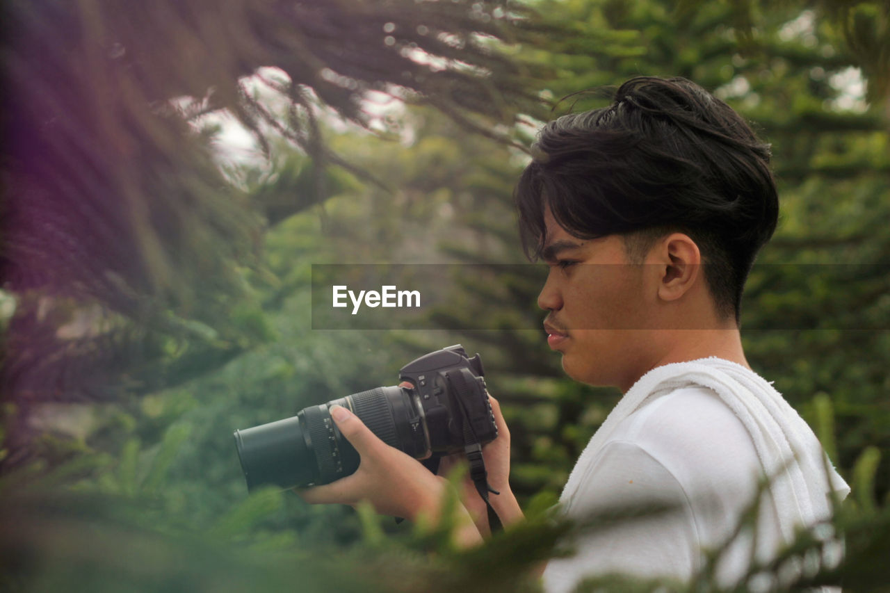 Side view of young man photographing in forest