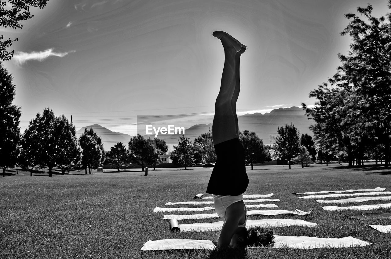 Side view of young woman doing handstand on grassy field