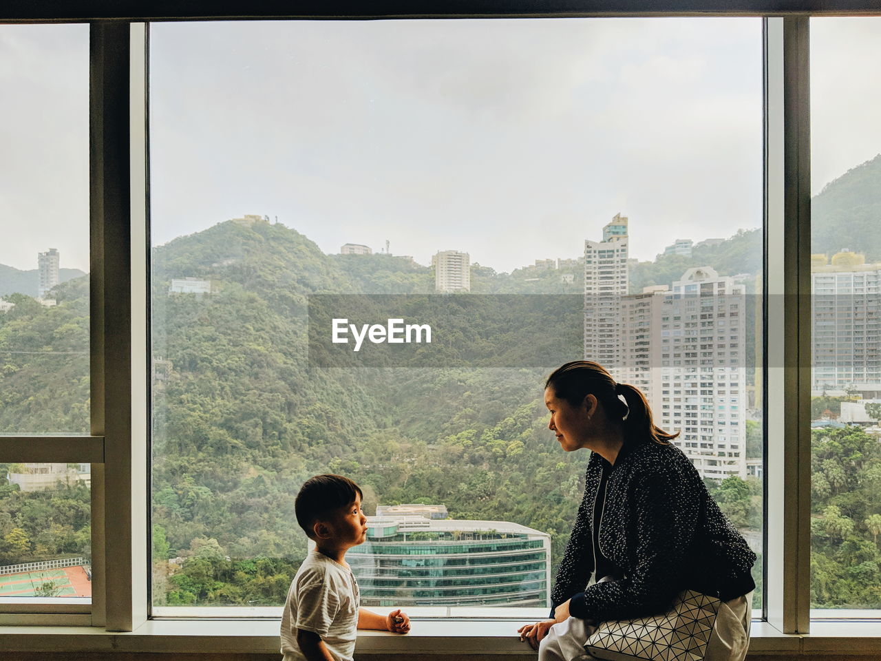 Mother talking with son while sitting on window sill at home