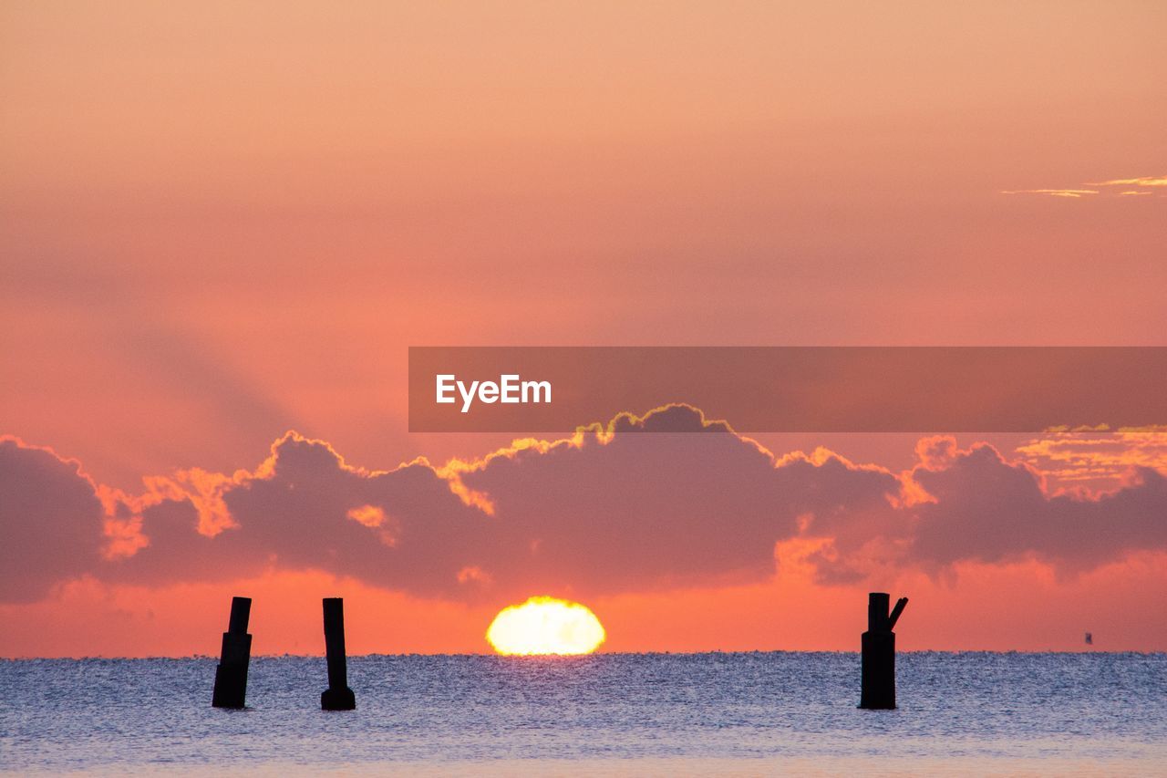 Silhouette wooden posts in sea against sky during sunset