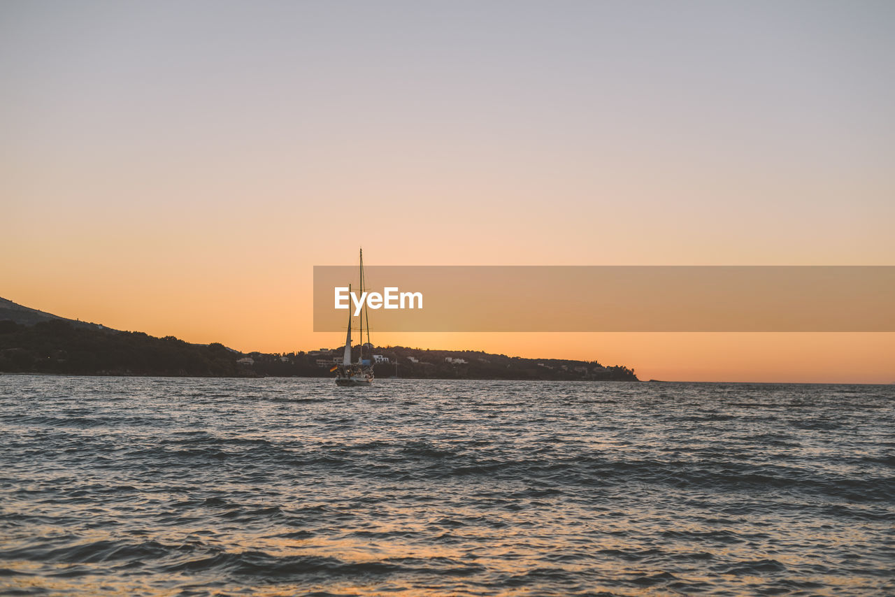 Sailboat sailing on sea against clear sky during sunset