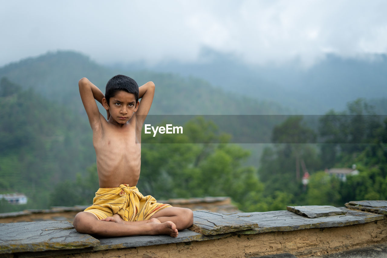 A young indian cute kid doing yoga in the mountains,wearing a dhoti