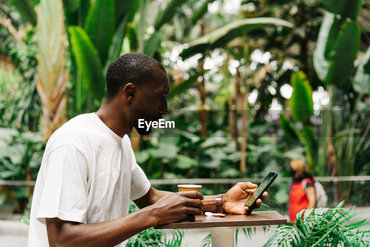 MAN LOOKING AT CAMERA WHILE USING SMART PHONE OUTDOORS