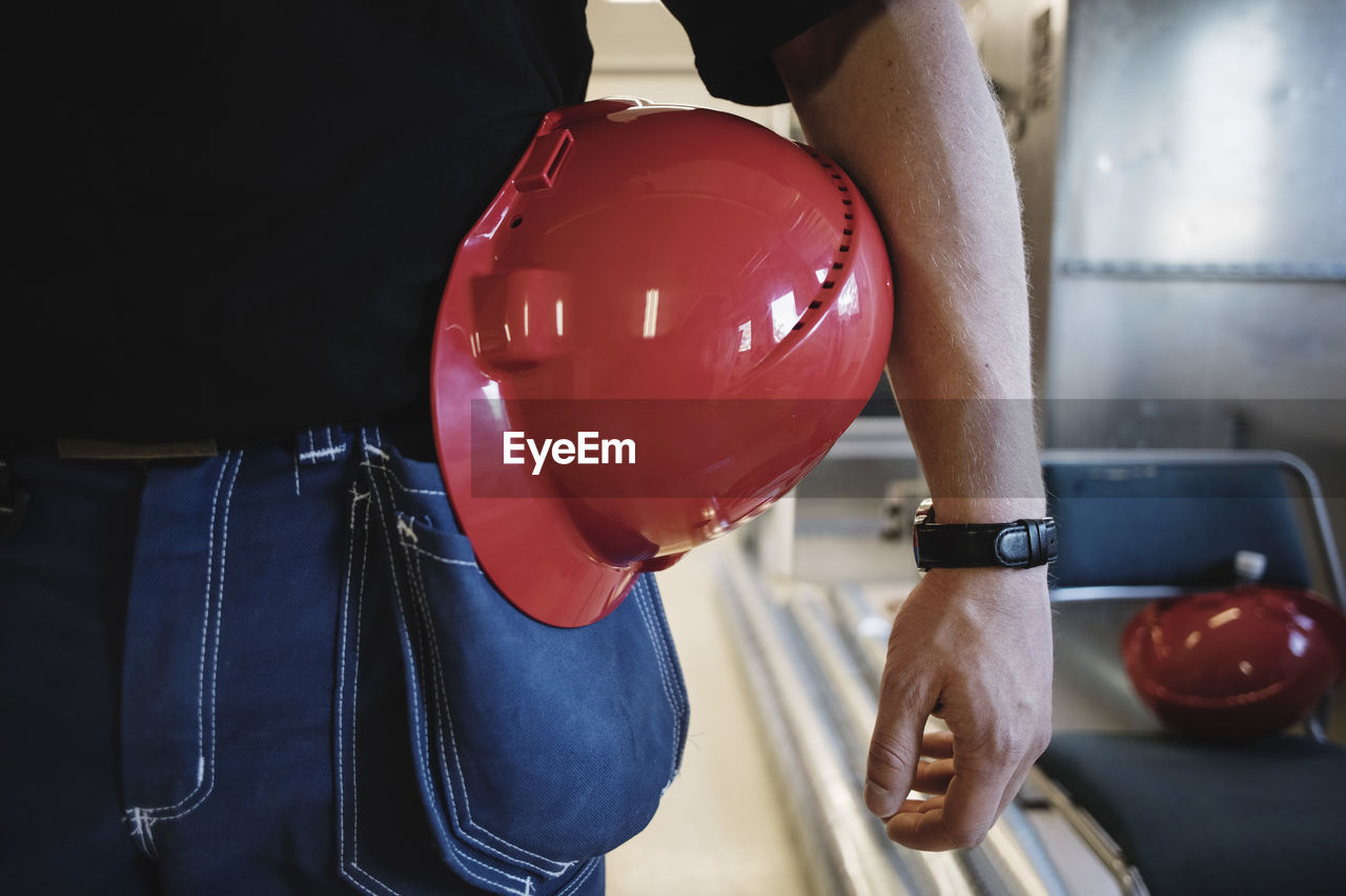 Midsection of auto mechanic teacher with red hardhat while standing at workshop