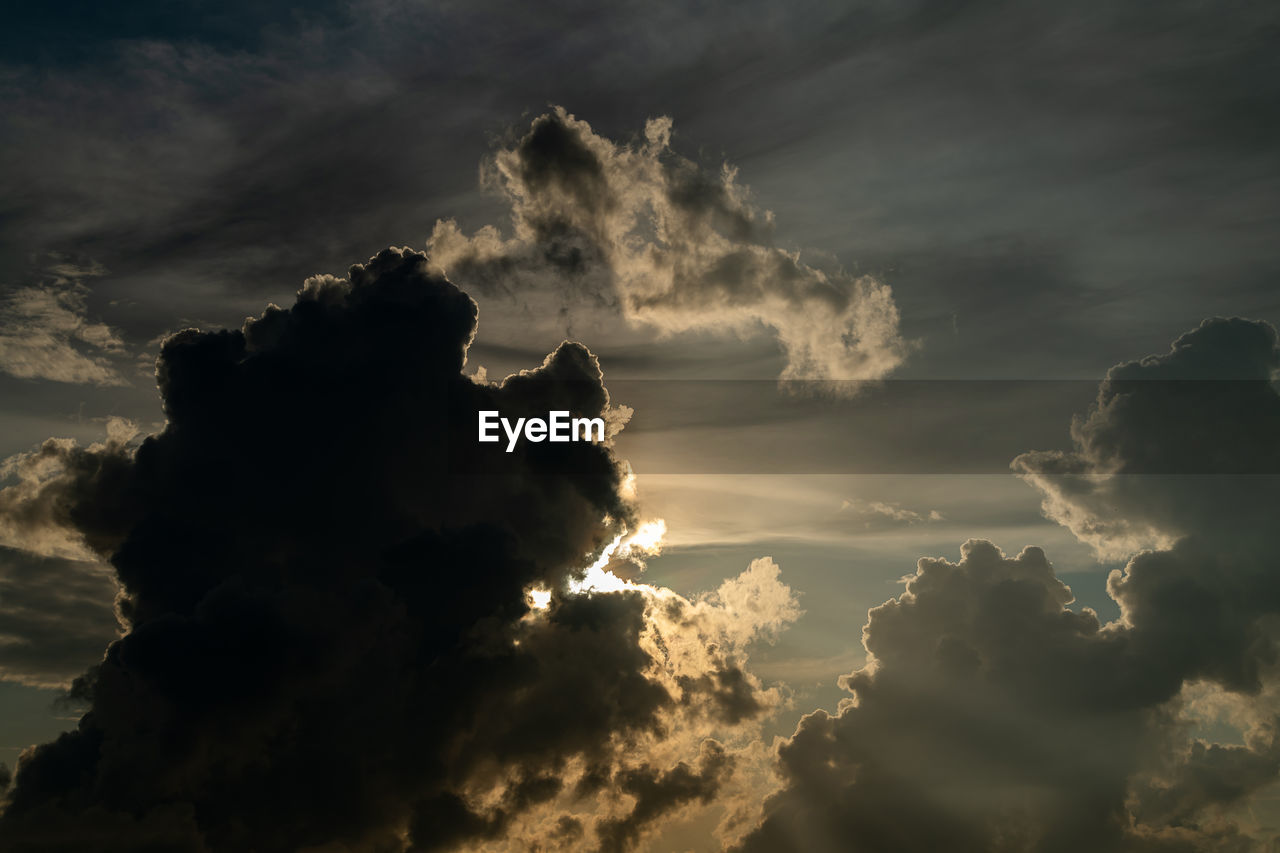 LOW ANGLE VIEW OF SUN STREAMING THROUGH CLOUDS DURING SUNSET