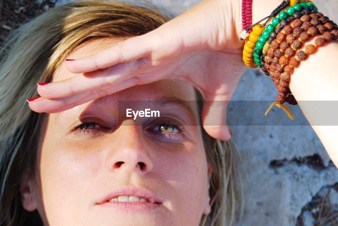 Close-up portrait of beautiful woman shielding eyes against wall on sunny day