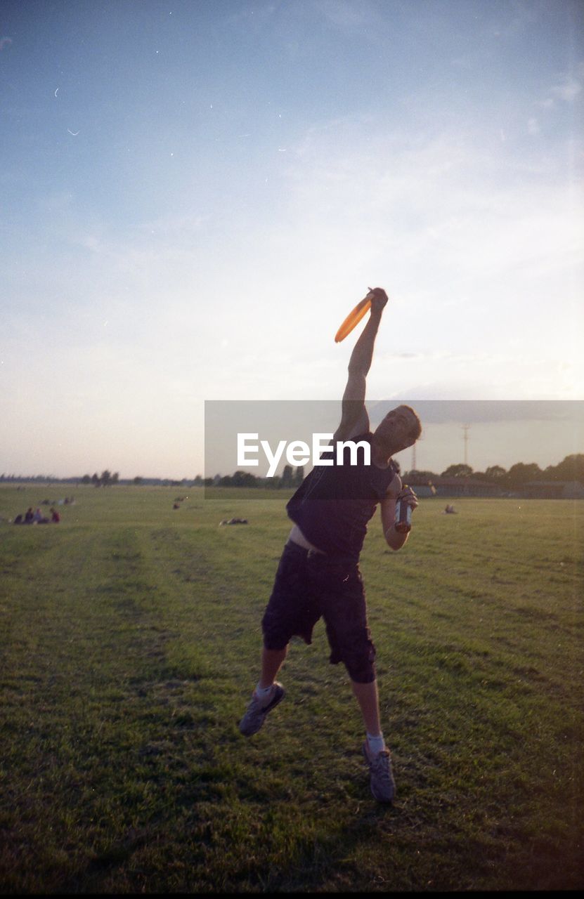 YOUNG MAN JUMPING ON GRASS AGAINST SKY