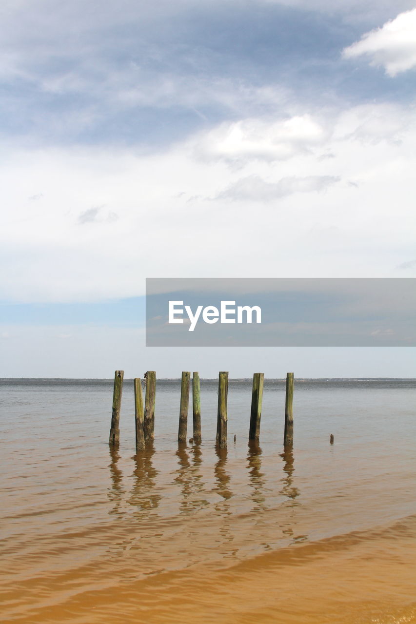 Wooden posts in sea against sky