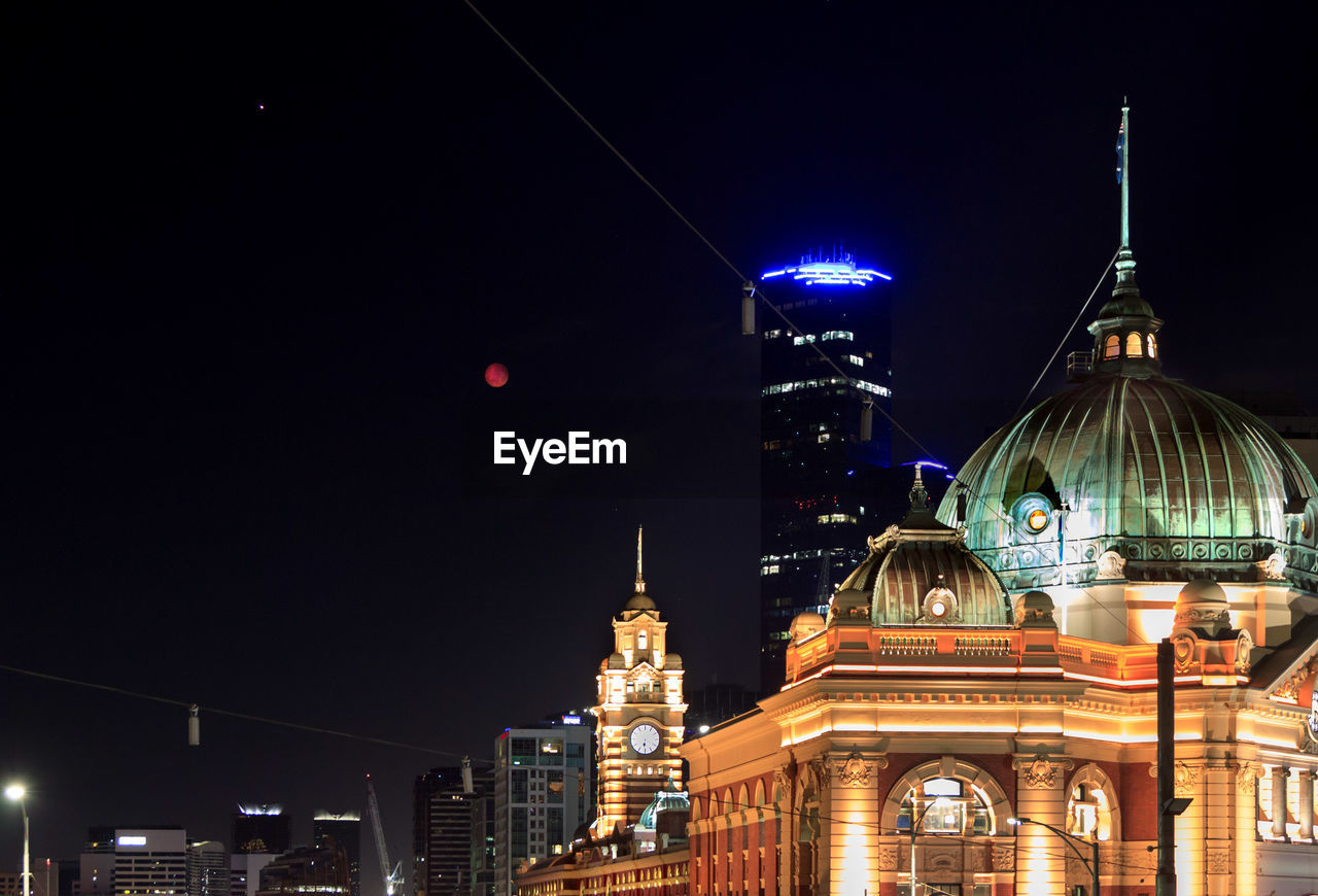 Illuminated flinders street station, buildings in city and super moon at night