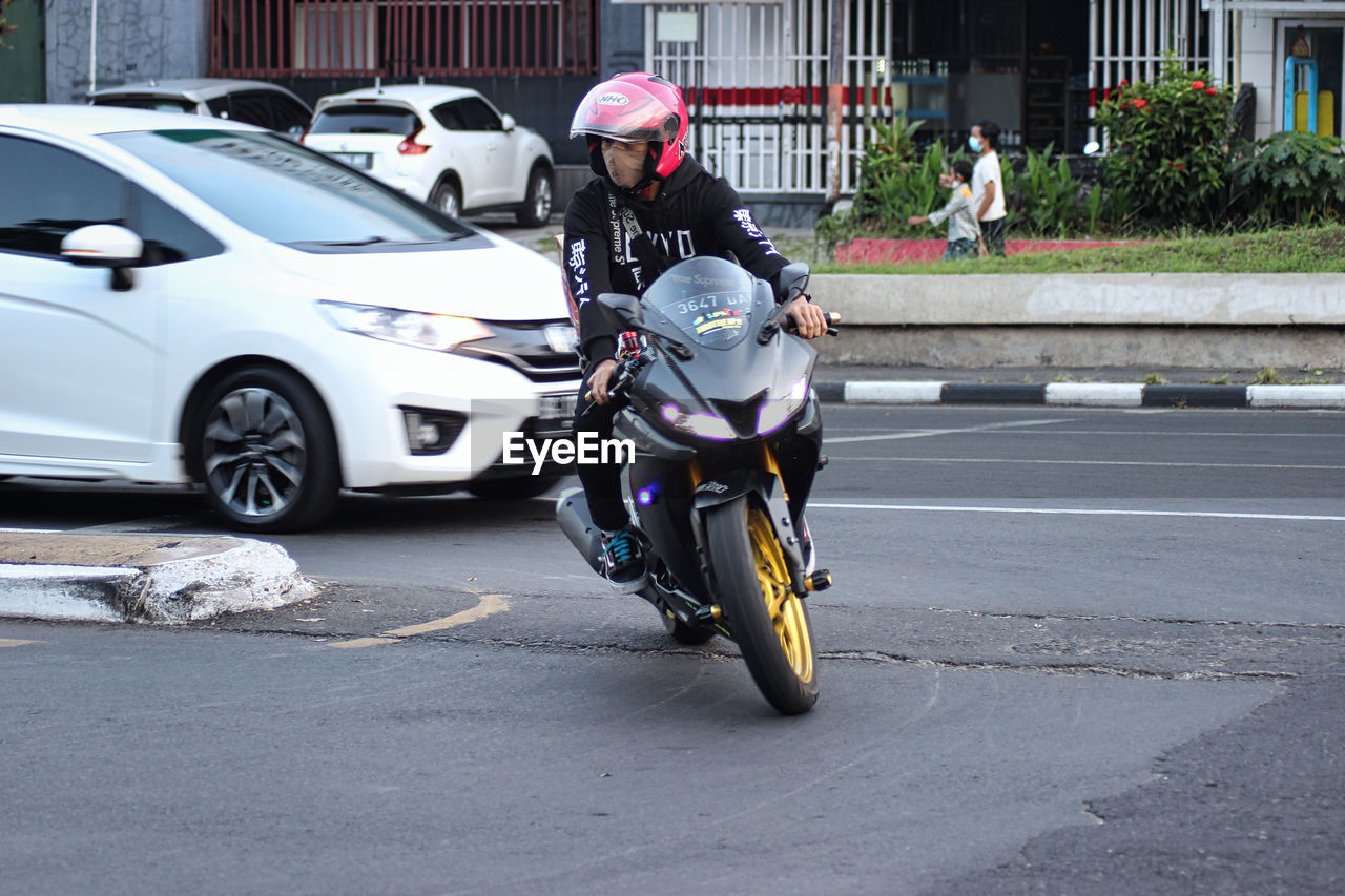 MAN RIDING MOTORCYCLE ON ROAD IN CITY