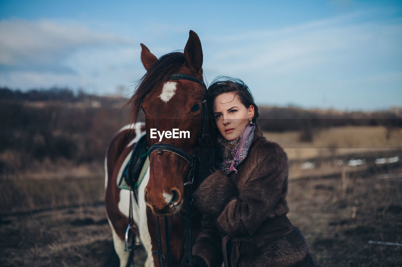 Beautiful young woman with horse standing on field