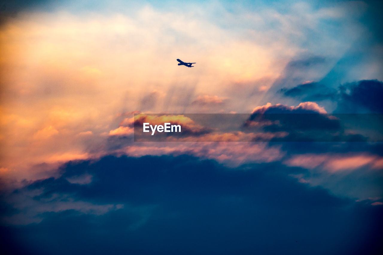 Low angle view of silhouette airplane flying in cloudy sky during sunset