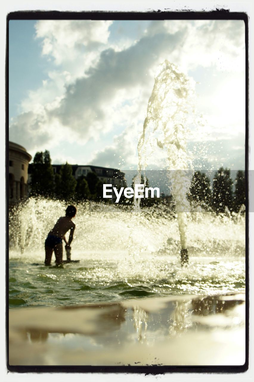 Silhouette boy enjoying in fountain against sky on summer sunset