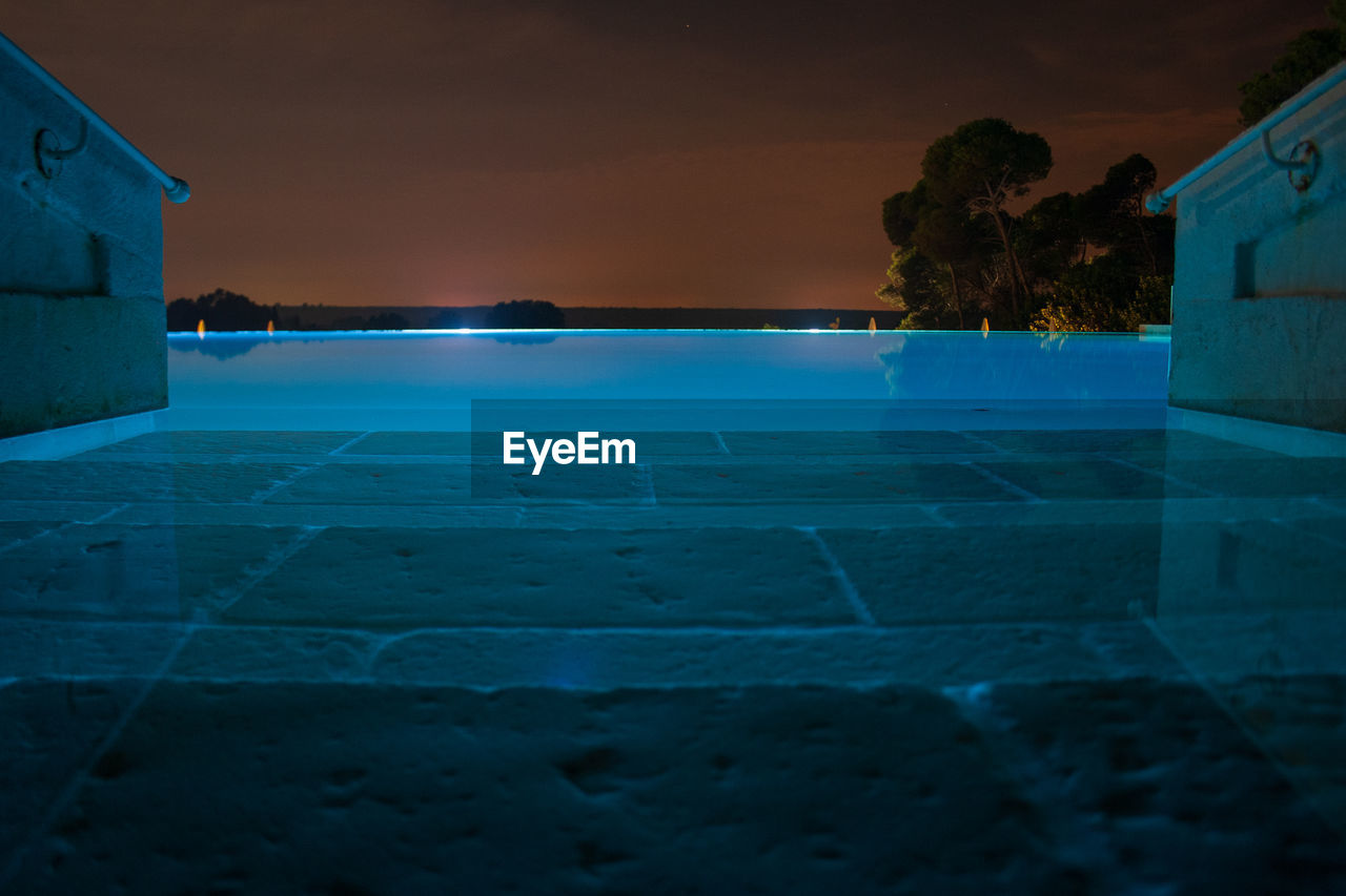 VIEW OF SWIMMING POOL BY BUILDING AT NIGHT