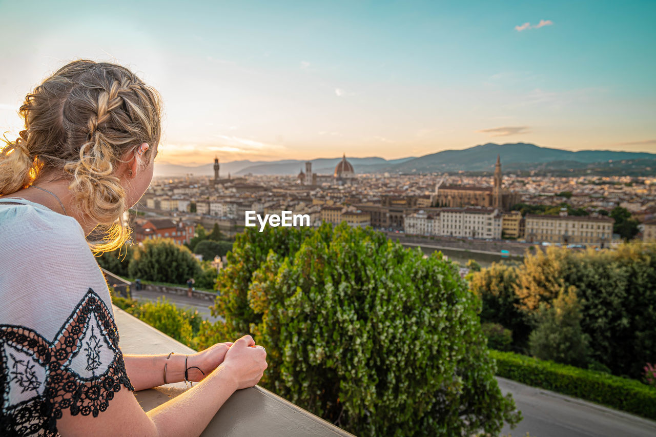 MAN SITTING BY CITYSCAPE AGAINST SKY