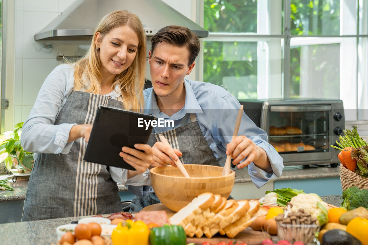 A woman and a man who are lovers are happy to help each other bake.