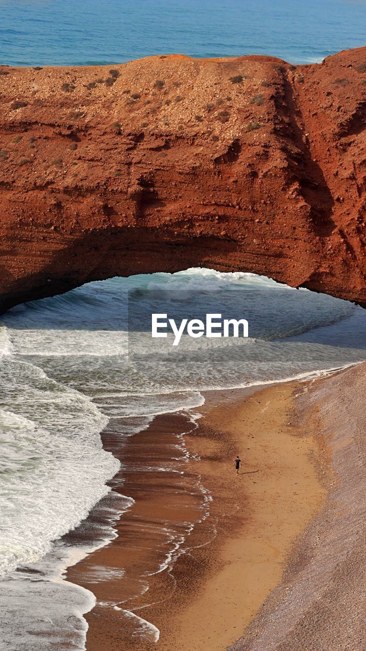 Contrast of giant legzira stone arch and small person on seaside