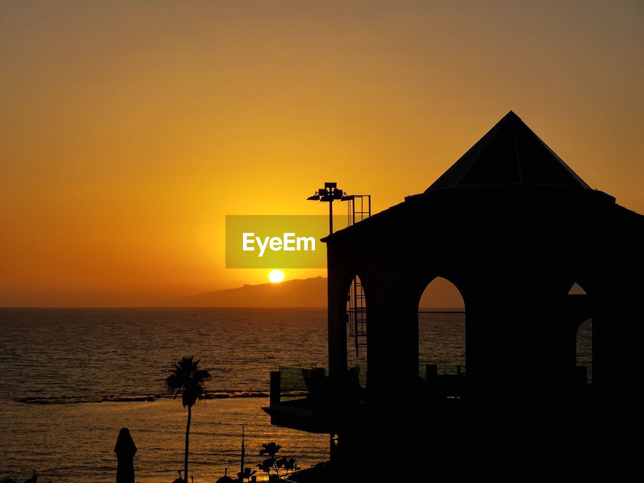 SILHOUETTE BUILT STRUCTURE AGAINST SEA DURING SUNSET