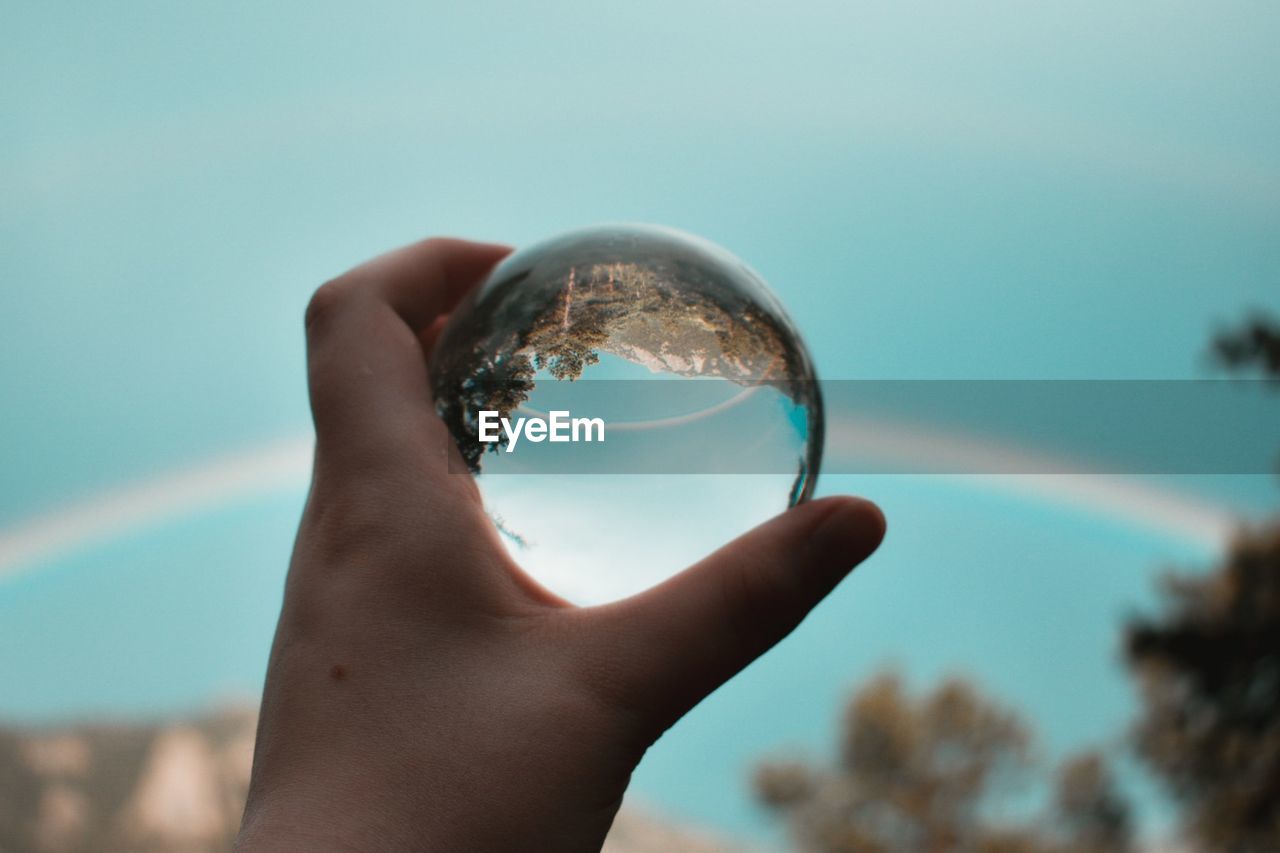 Close-up of hand holding crystal ball against sky