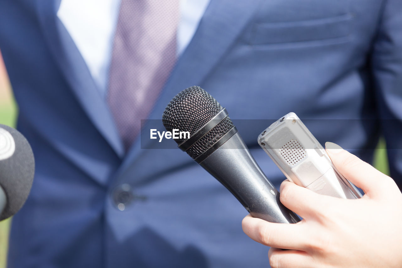 Midsection of businessman standing by microphones