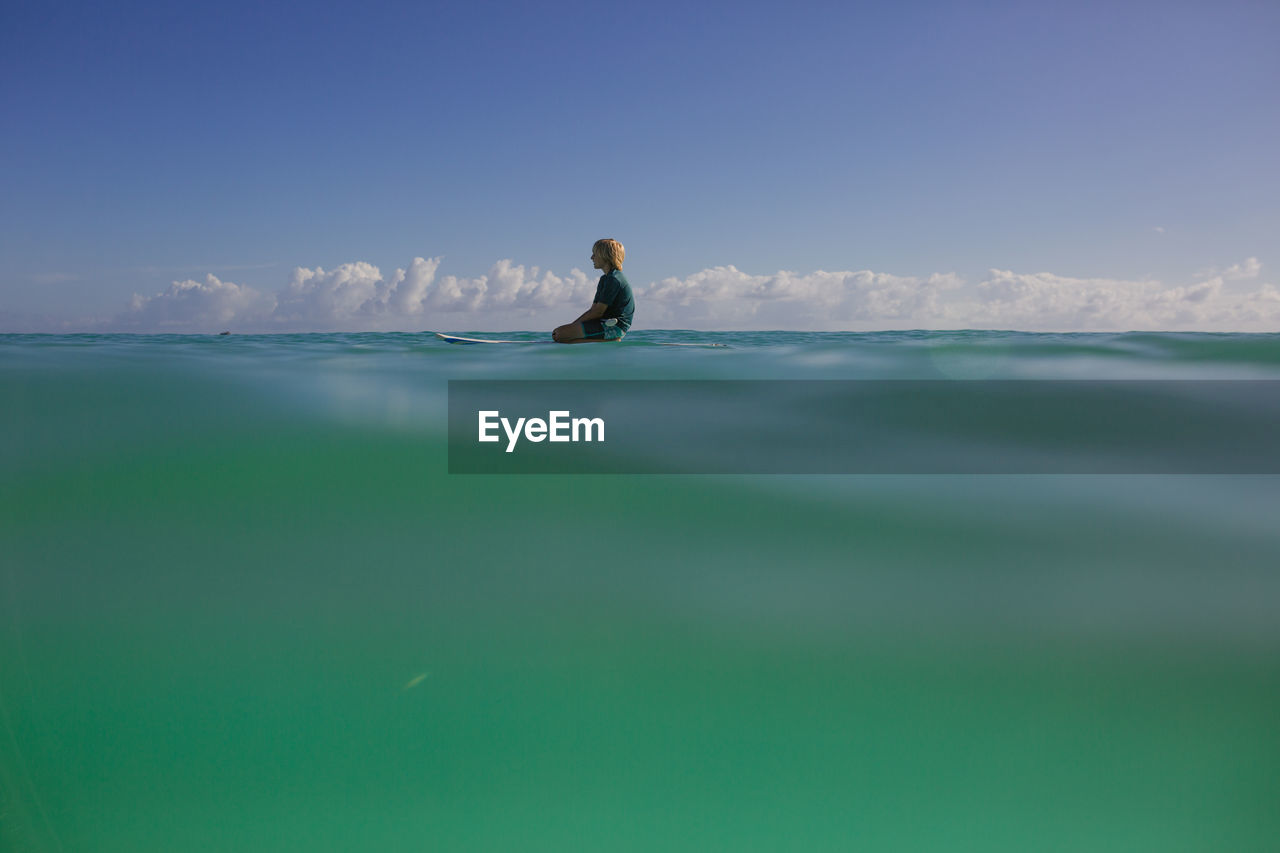 Boy rests on a paddleboard on a calm day with turquoise water.