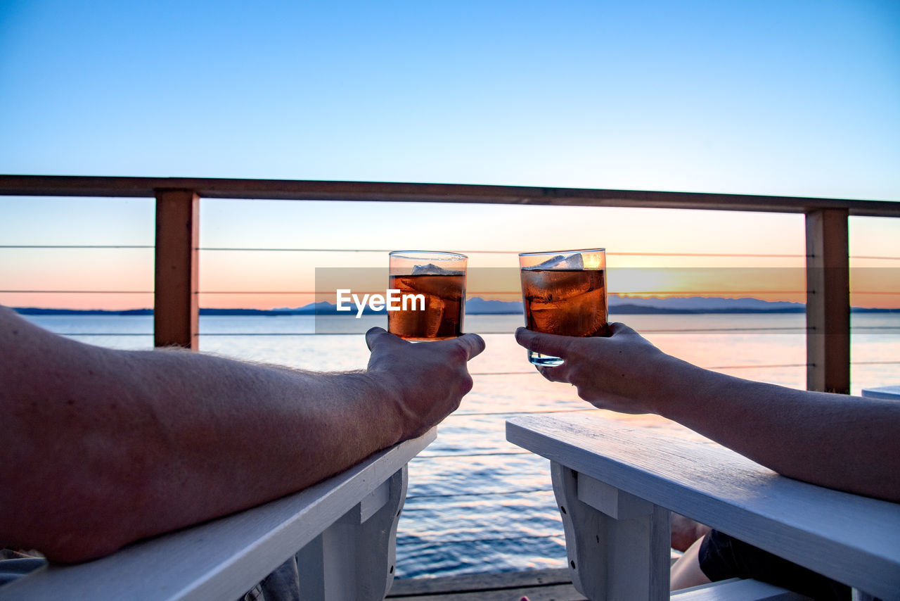 Cropped image of couple drinking whiskey on pier against sky
