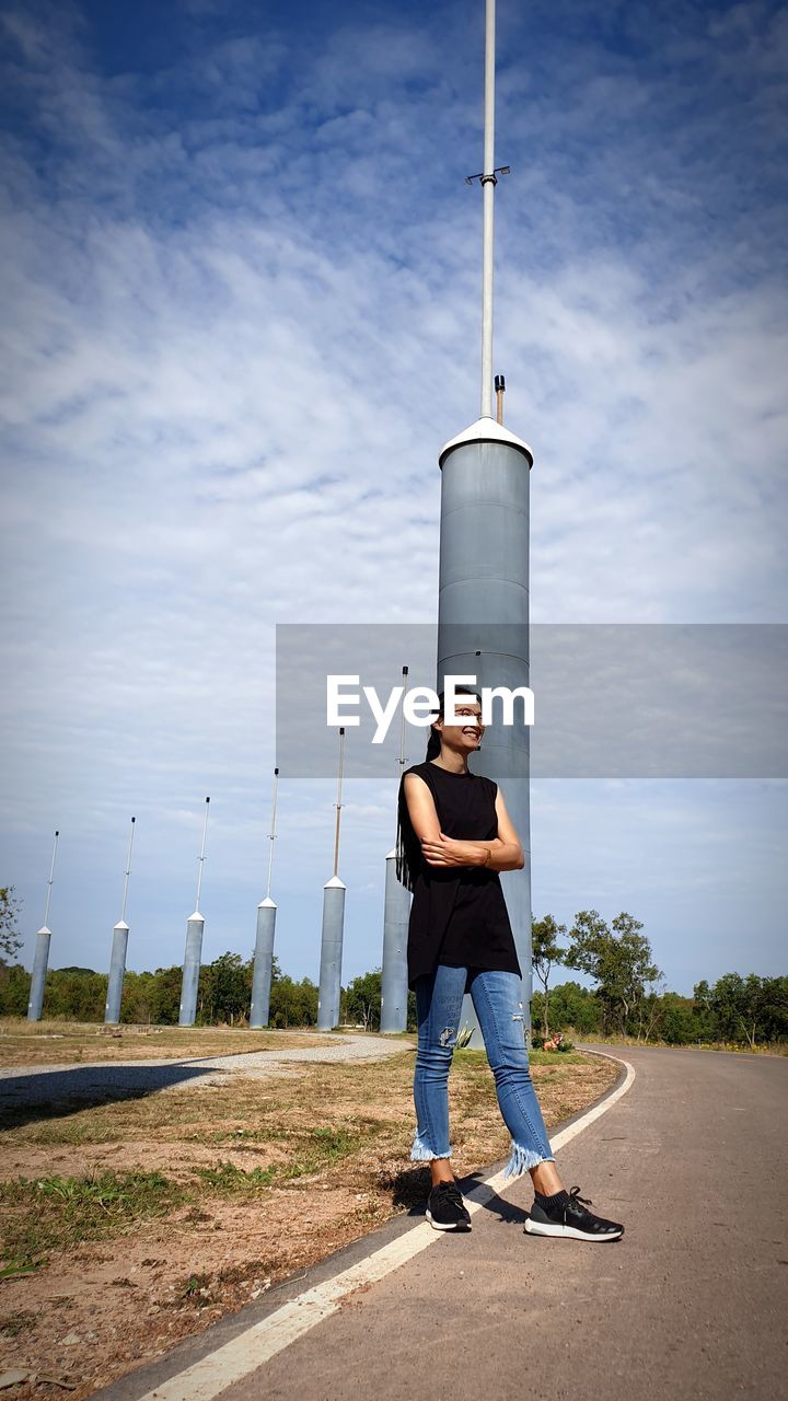 Full length of young woman standing on road against sky