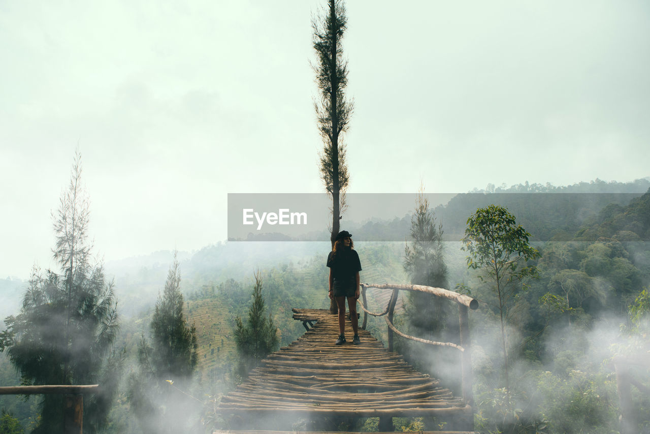 Woman  standing on footbridge against sky