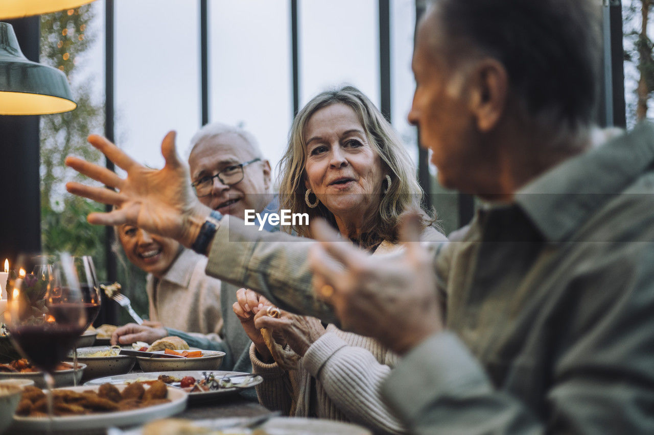 Senior woman listening to male friend gesturing while talking at dinner party