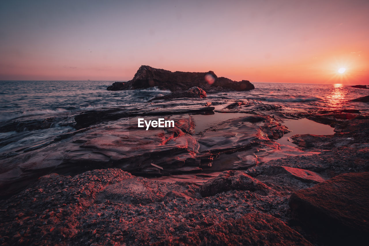 SCENIC VIEW OF ROCKS ON SEA AGAINST SKY DURING SUNSET