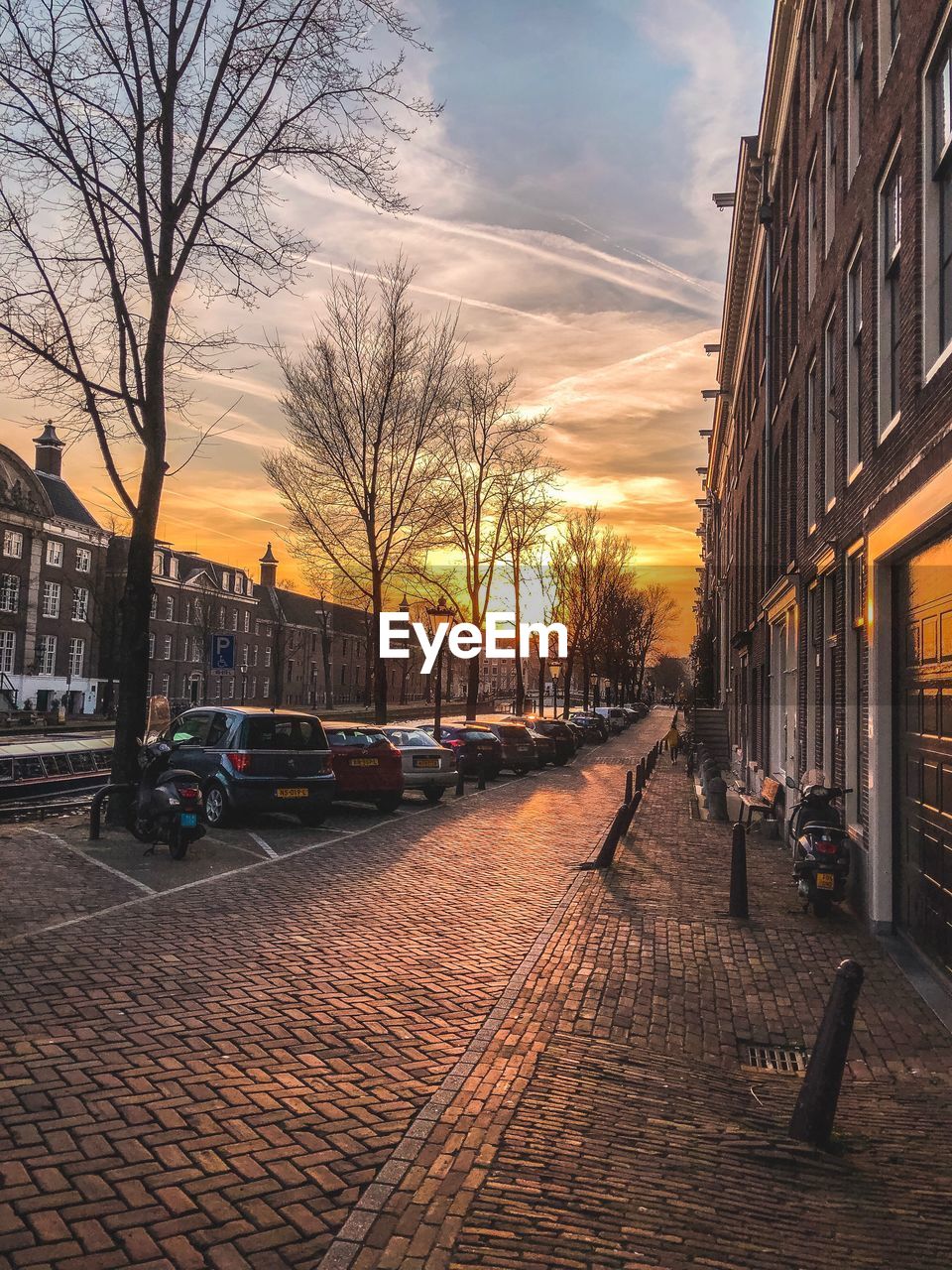 STREET AMIDST BUILDINGS AGAINST SKY DURING SUNSET