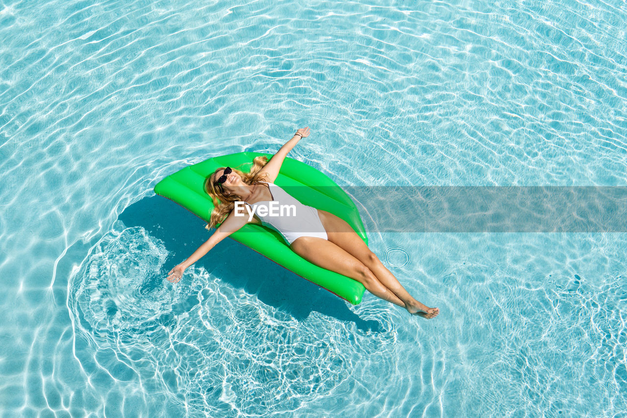 From above full body smiling female in white one piece suit chilling on air mattress on pool water on hot sunny day