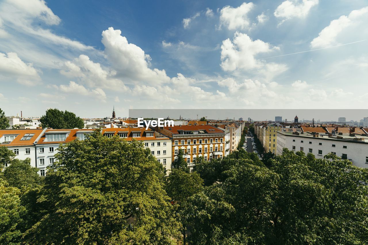 Trees and buildings against cloudy sky