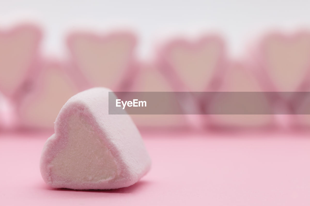 Close-up of pink heart shaped marshmallows on table against white background