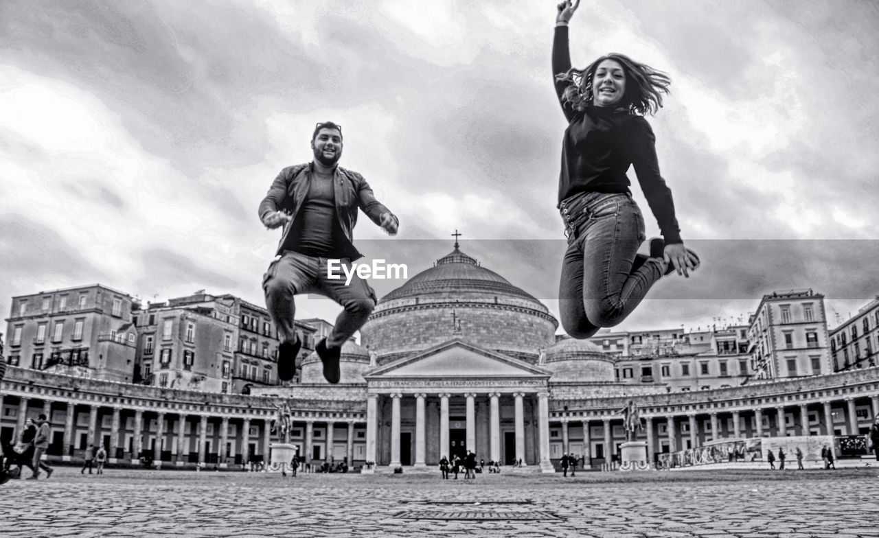 Smiling friends jumping over footpath in city