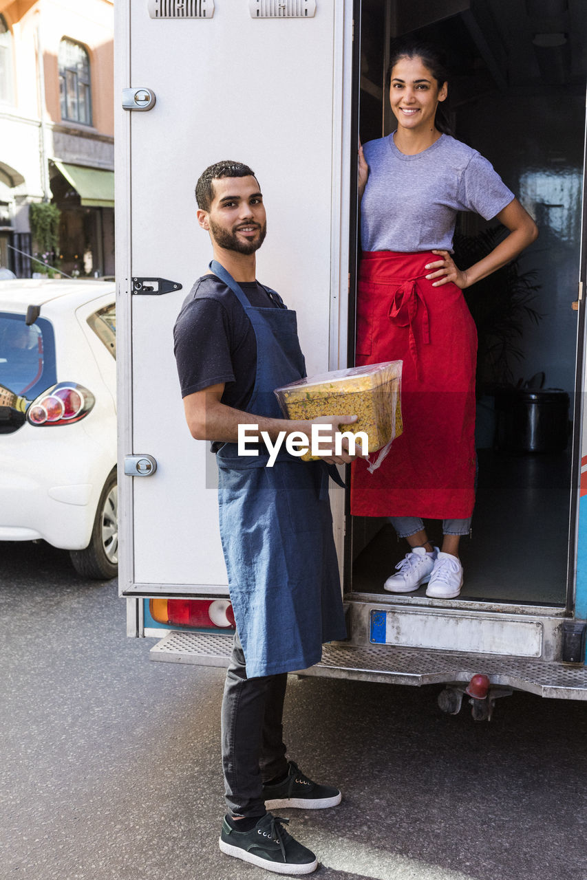 Full length portrait of confident young multi-ethnic colleagues standing at food truck in city