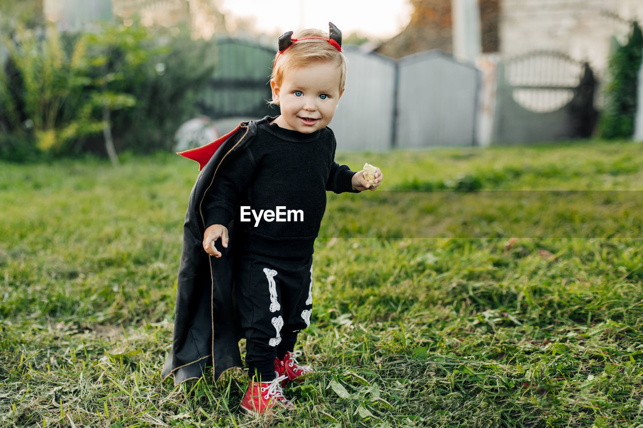 A charming kid in a devil costume and a raincoat sneaks around the garden. halloween concept