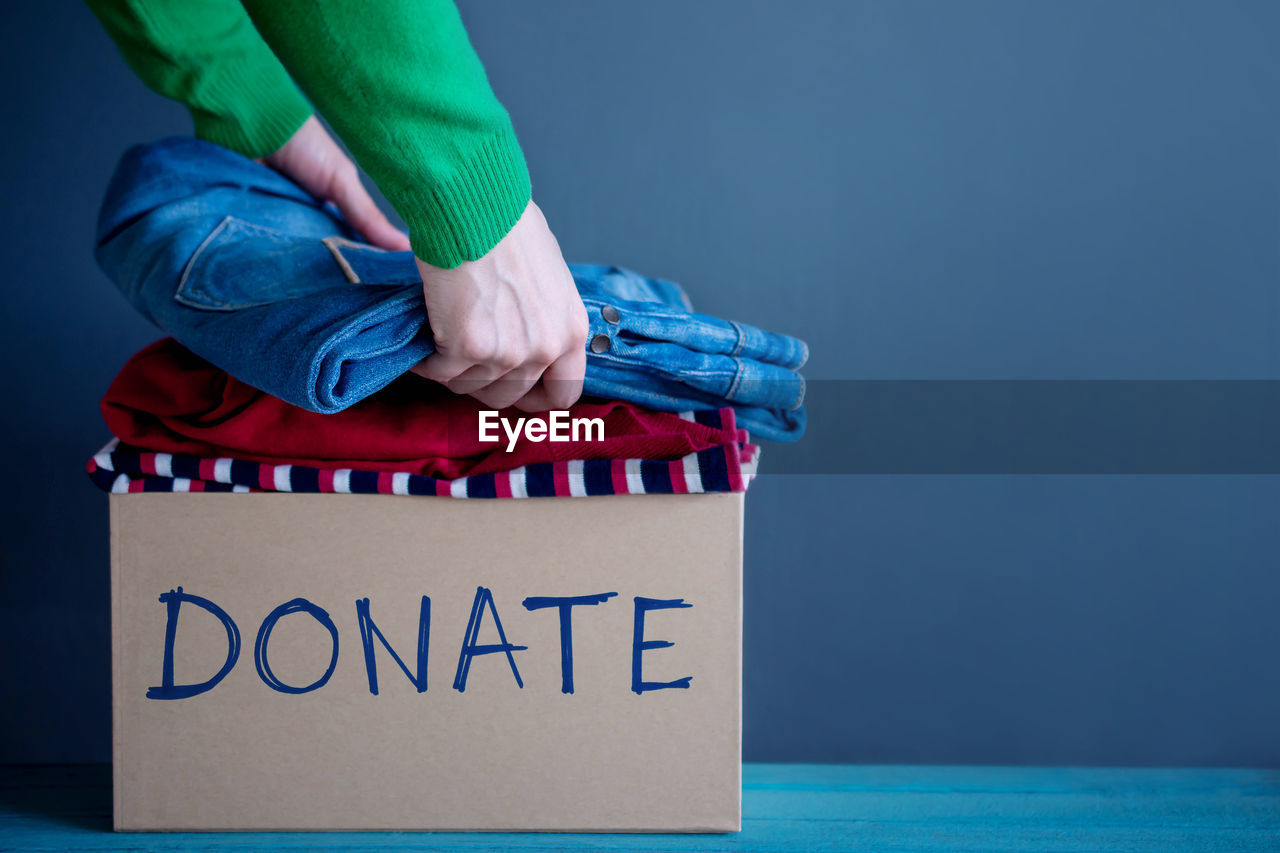 Cropped hands of woman with clothes in box with donate text