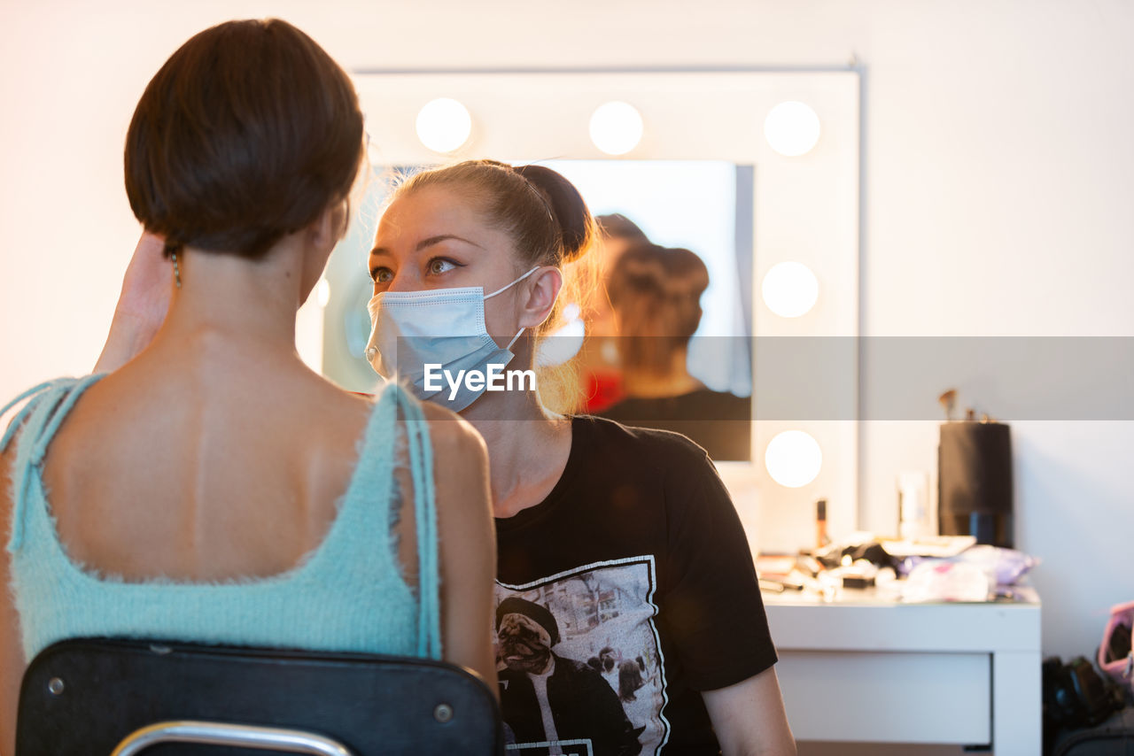 Female makeup artist applying foundation with brush on face of charming model sitting in salon