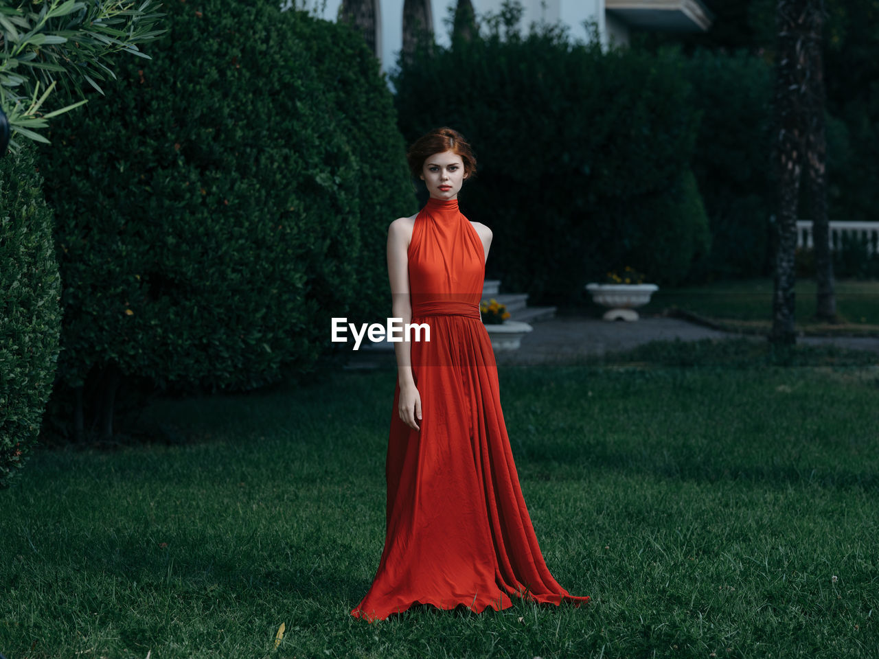 PORTRAIT OF YOUNG WOMAN STANDING BY PLANTS