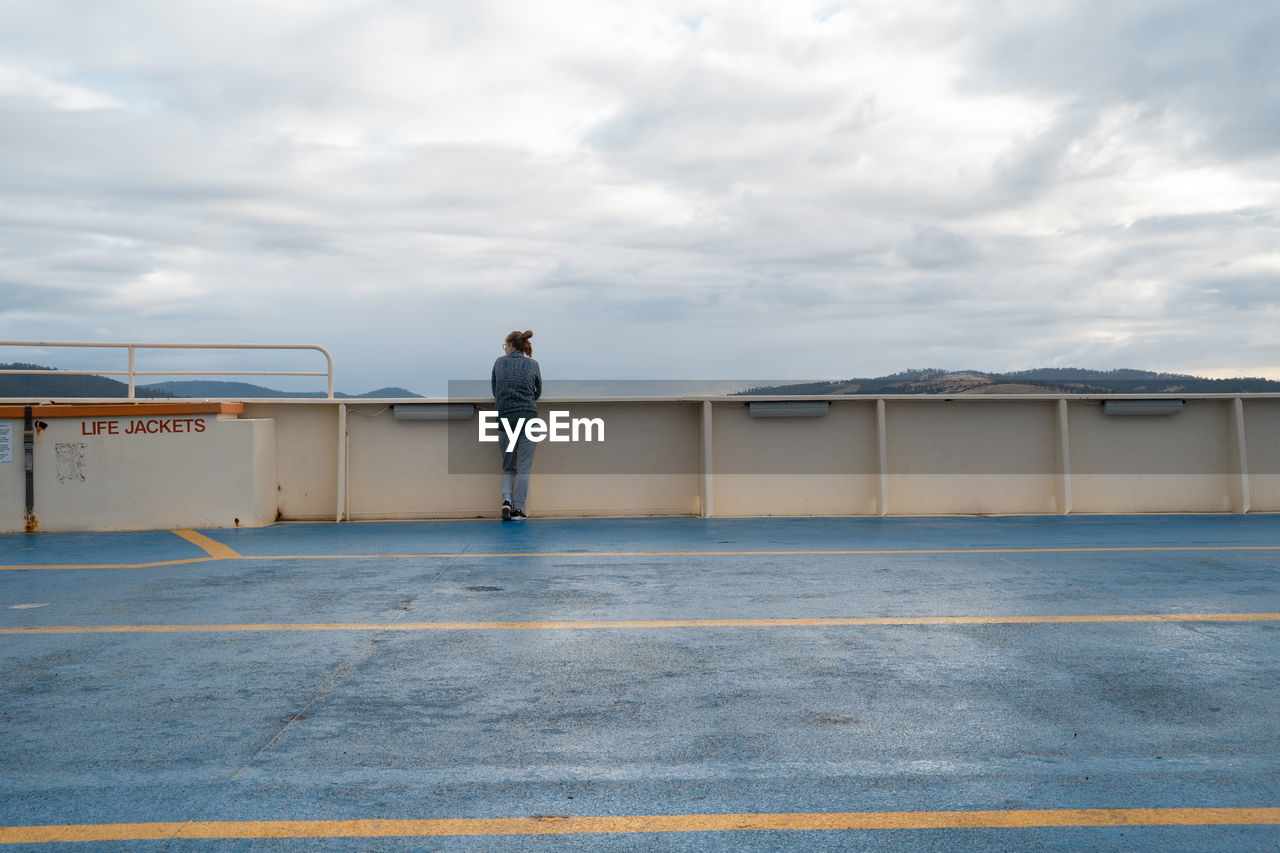 REAR VIEW OF MAN STANDING BY ROAD AGAINST SKY