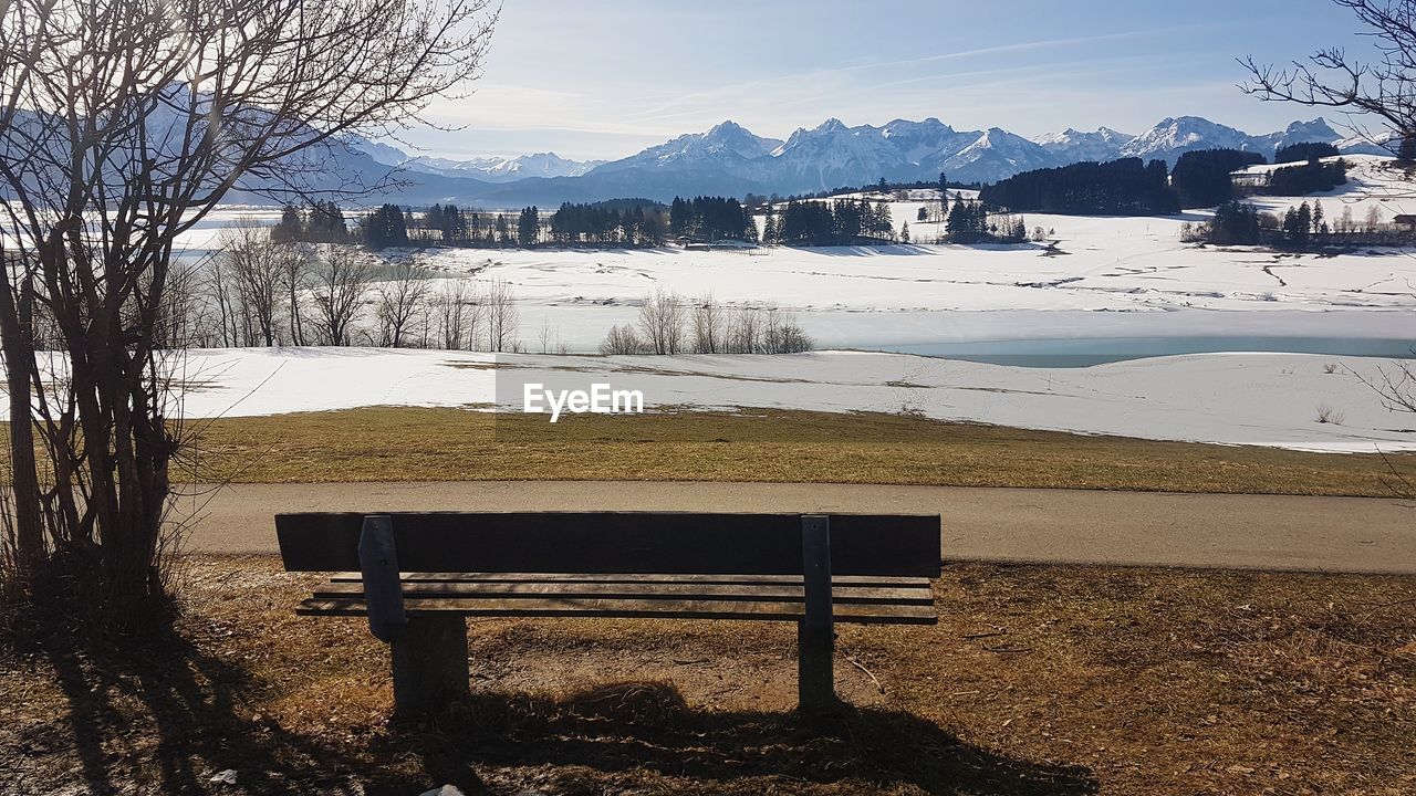 BENCH ON FIELD BY SNOWCAPPED MOUNTAIN AGAINST SKY
