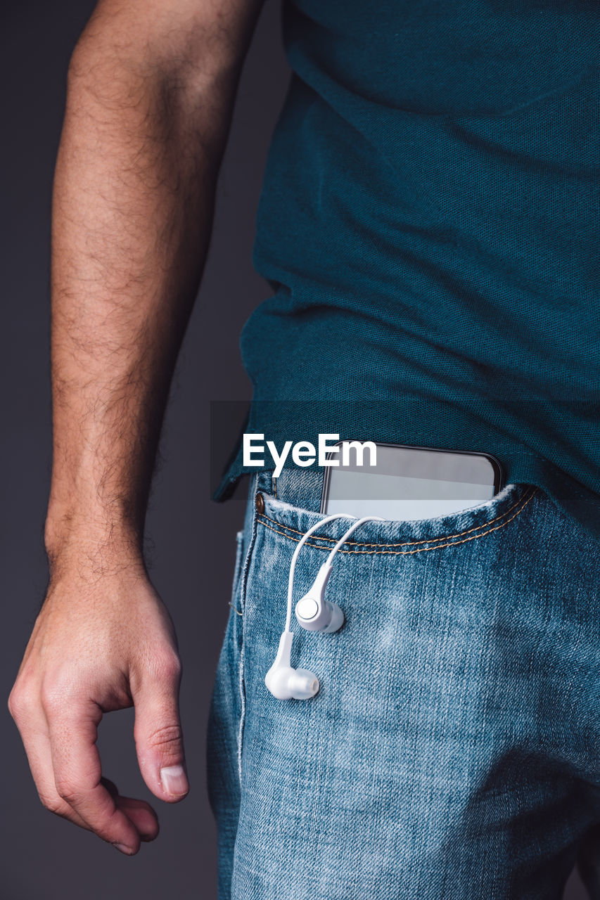Midsection of man with mobile phone and in-ear headphones in pocket