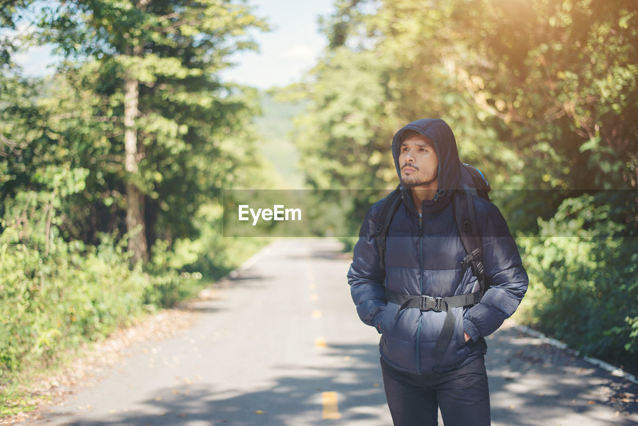 Thoughtful male hiker standing on road amidst trees