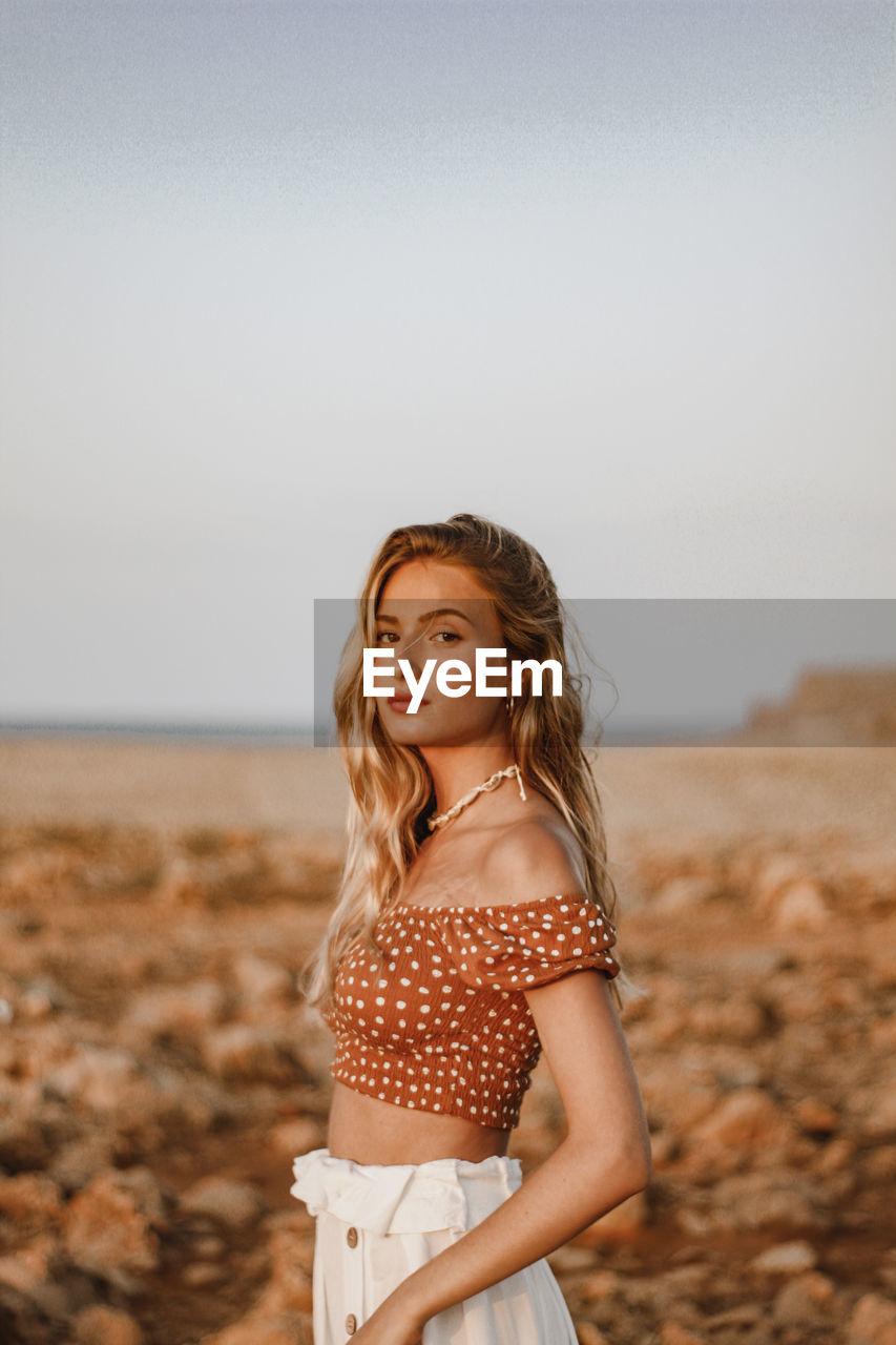 Portrait of beautiful woman standing at beach against sky