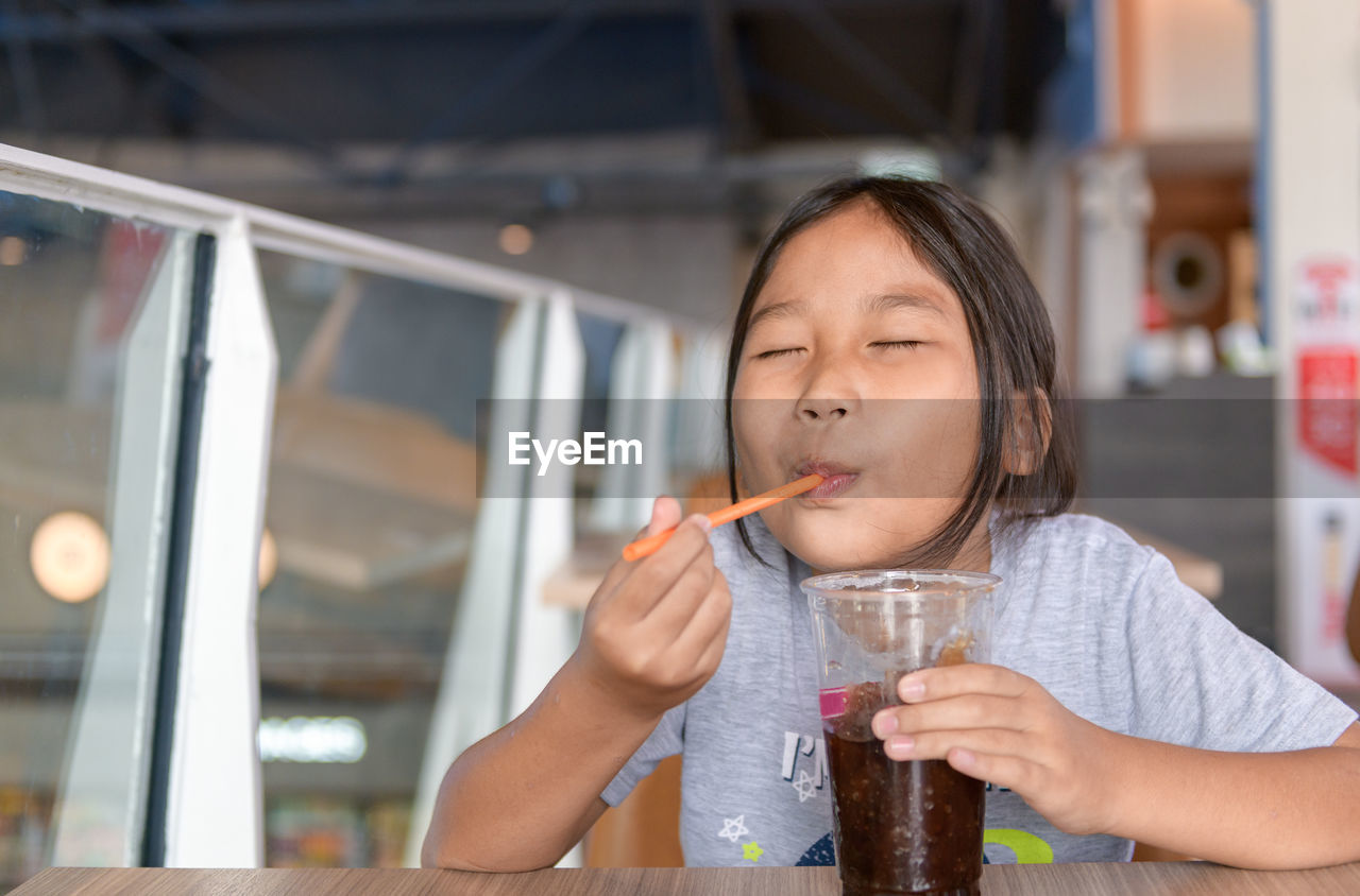 Happy girl drinking cola smoothie from plastic cup in convenience store, fast food concept