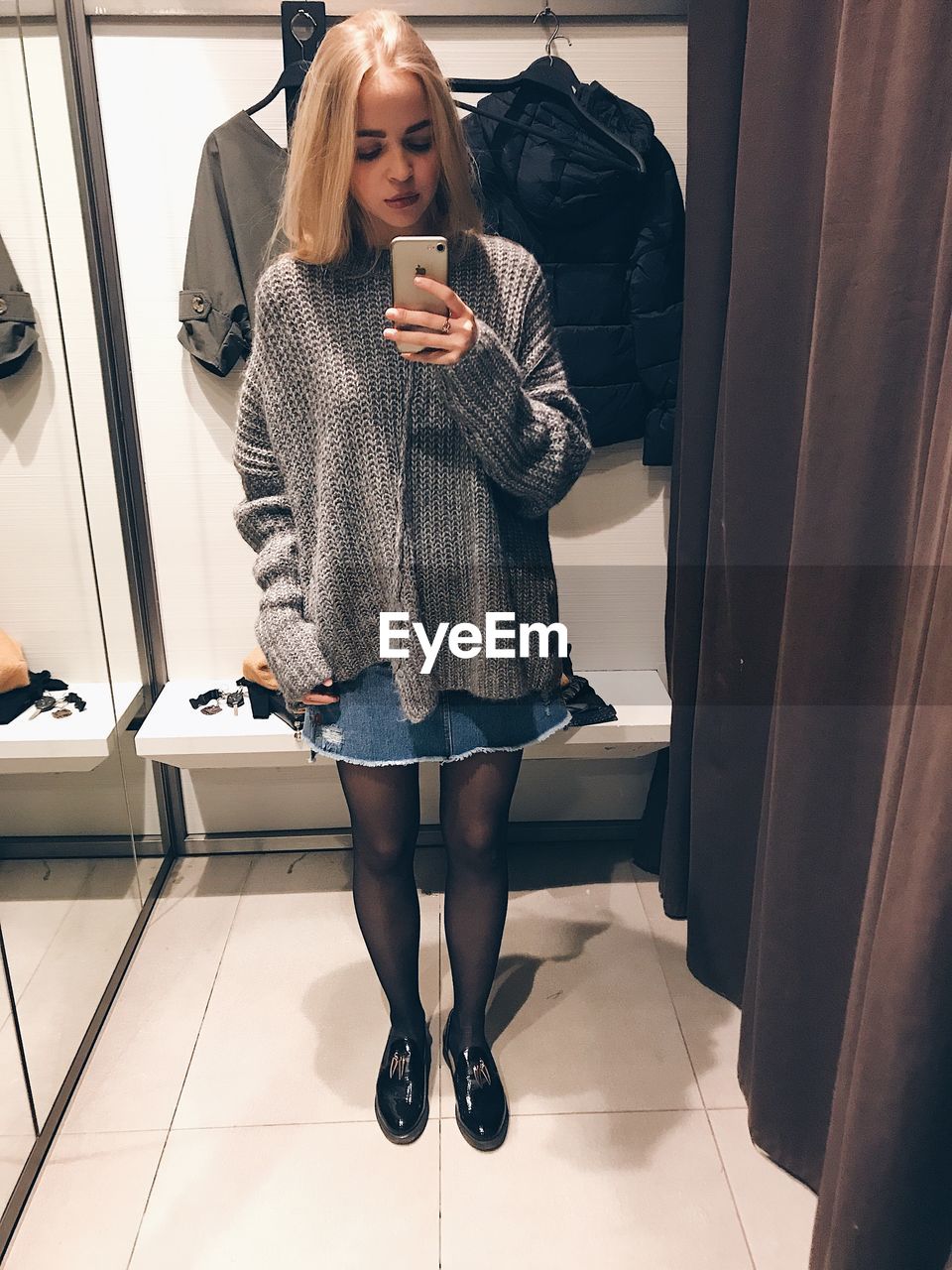 Full length of young woman taking selfie with smart phone while standing in store