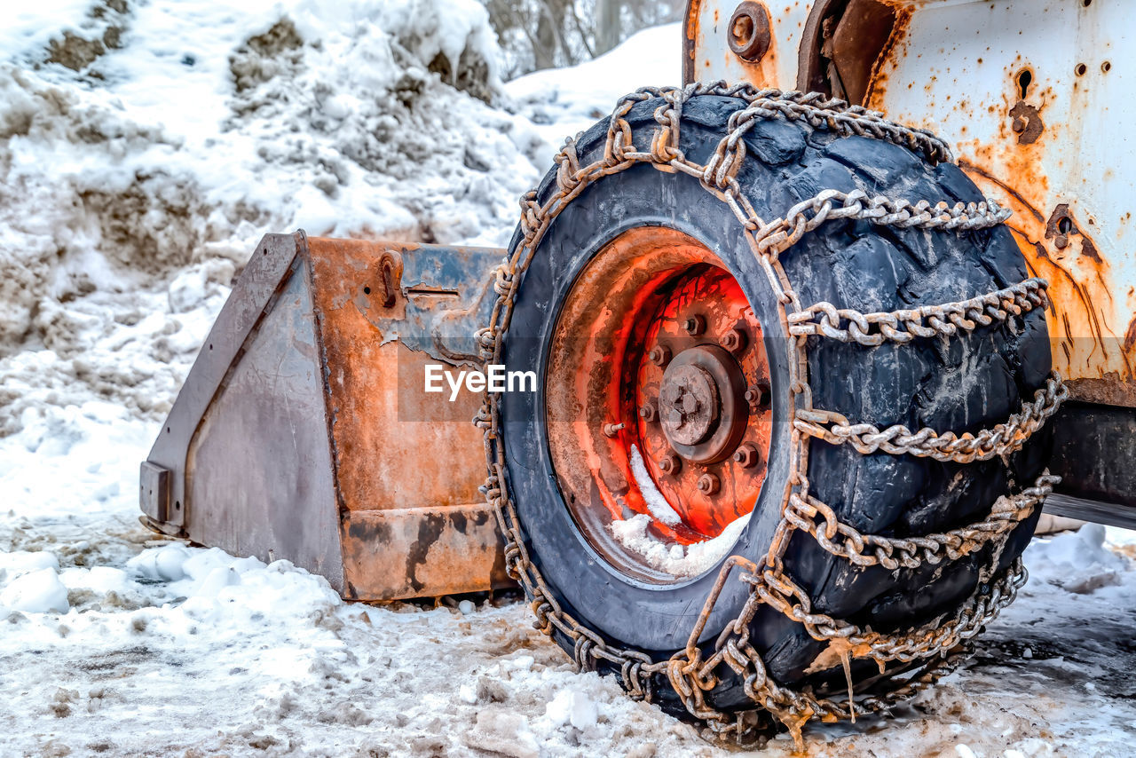 CLOSE-UP OF RUSTY WHEEL ON SNOW COVERED FIELD