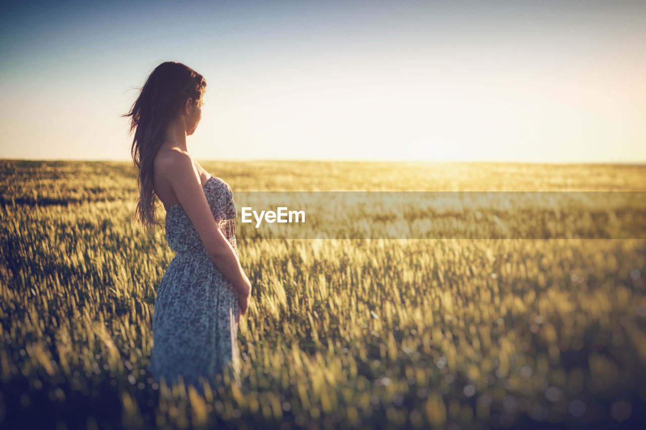 Side view of woman standing on grassy field against clear sky